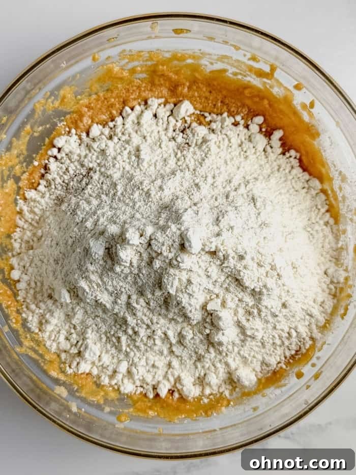 Adding flour and pumpkin in a mixing bowl for pumpkin spice cookies.