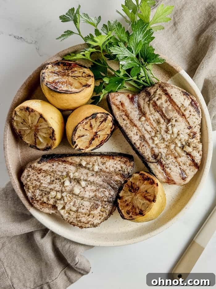 Grilled swordfish steak on a plate, garnished with lemon and herbs.
