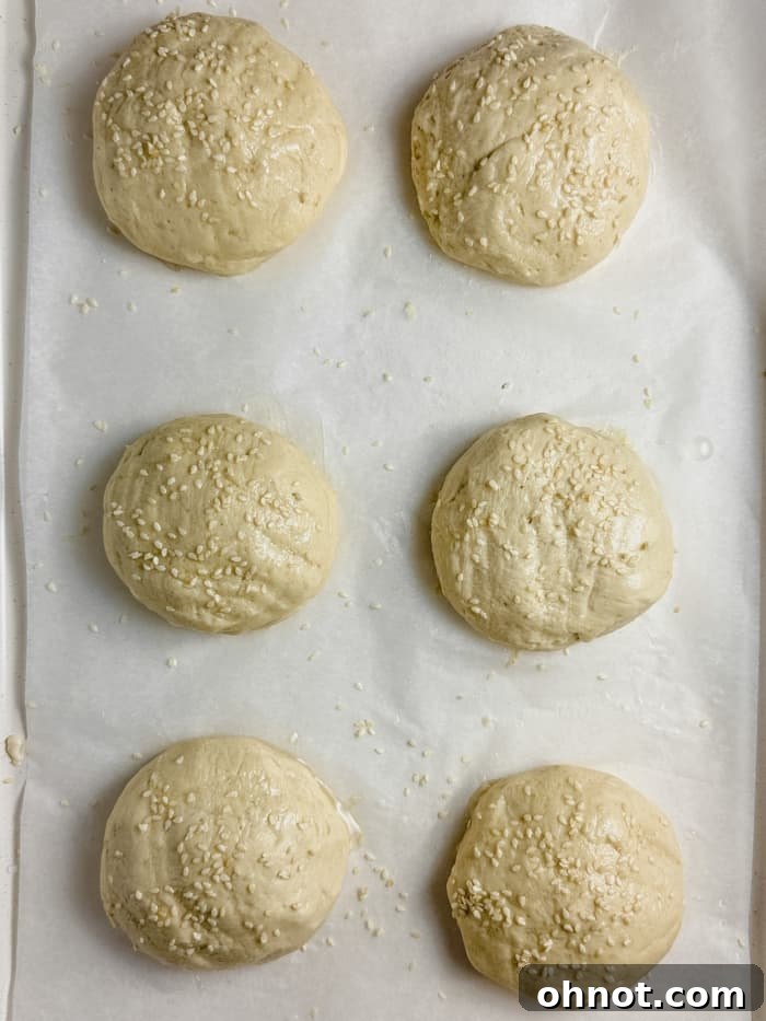 Unbaked gluten-free hamburger buns, shaped and topped with sesame seeds, ready for their second rise.