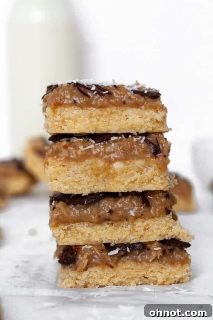 A stack of four perfectly layered Paleo Samoa bars on white parchment paper, with a glass of milk visible in the soft-focus background.