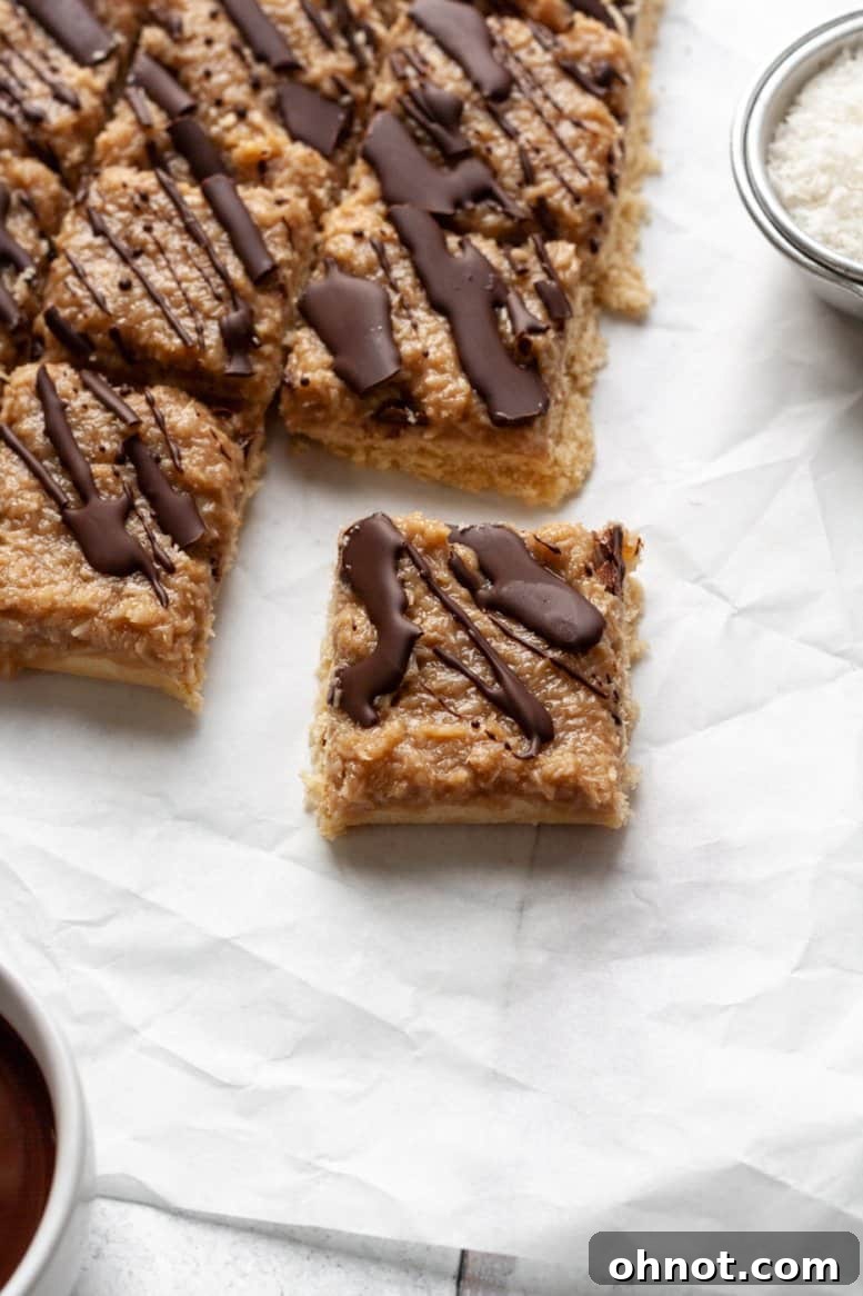 A close-up overhead shot of several Paleo Samoa bars arranged artfully on white parchment paper, highlighting their distinct layers of shortbread, caramel, coconut, and chocolate drizzle.
