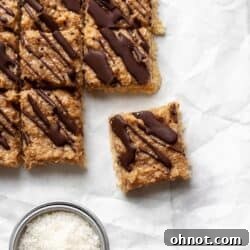 Samoa bars on white parchment paper with a measuring cup filled with coconut flakes.