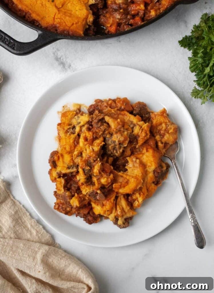 A serving of Whole30 Shepherd's Pie on a white plate with a side of fresh herbs.