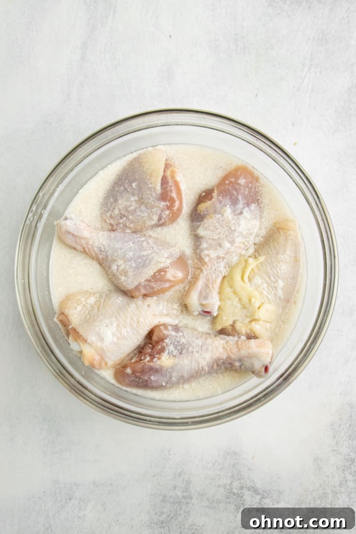 Chicken drumsticks marinating in buttermilk in a large mixing bowl.