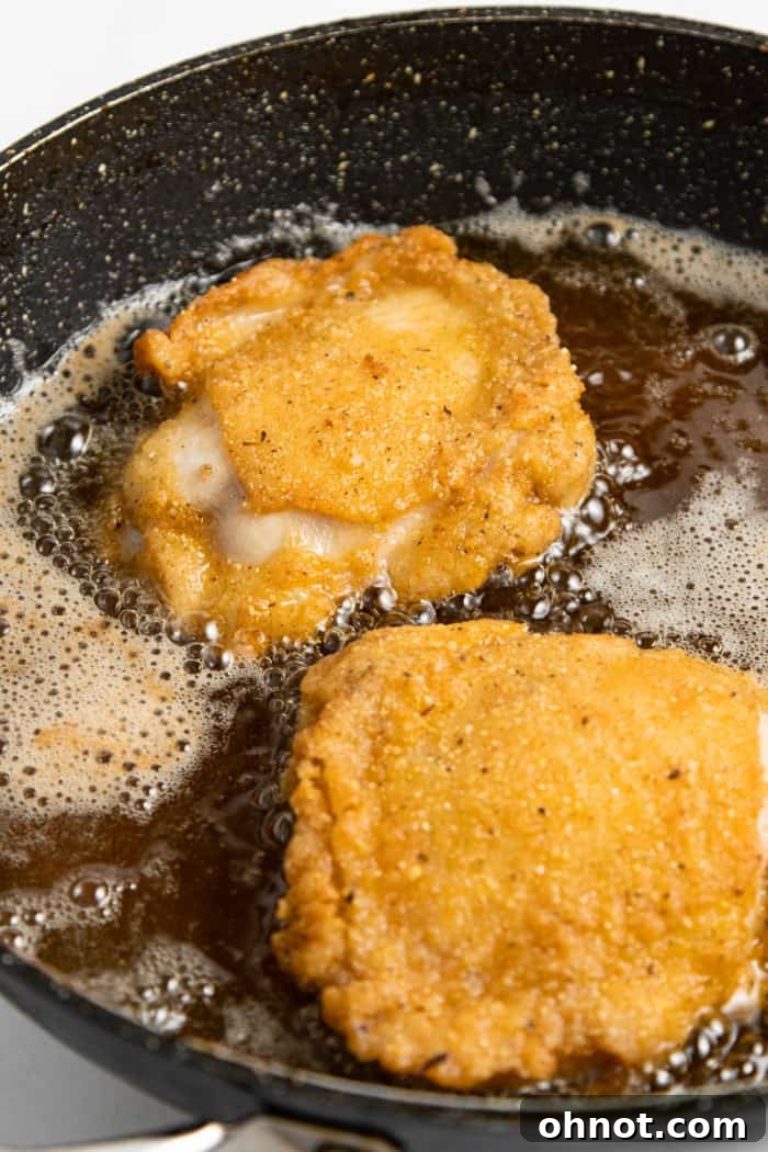 Gluten-free fried chicken pieces sizzling in hot oil in a large skillet.