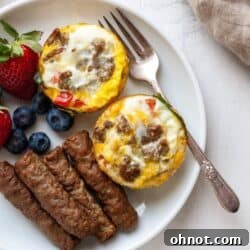Whole30 Egg muffins on a white plate with air fryer sausage and fruit, showcasing a perfect healthy breakfast.