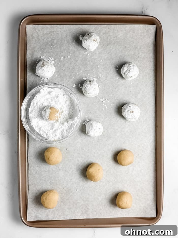Dough balls generously coated in powdered sugar and placed on a baking sheet.
