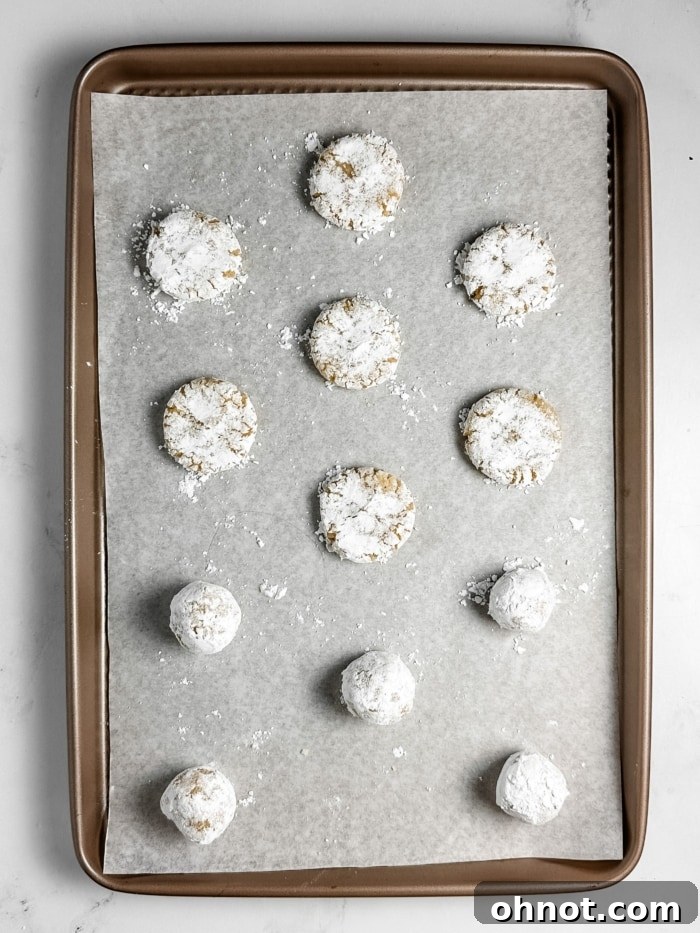 Flattened, powdered sugar-coated cookies on parchment-lined baking pan.