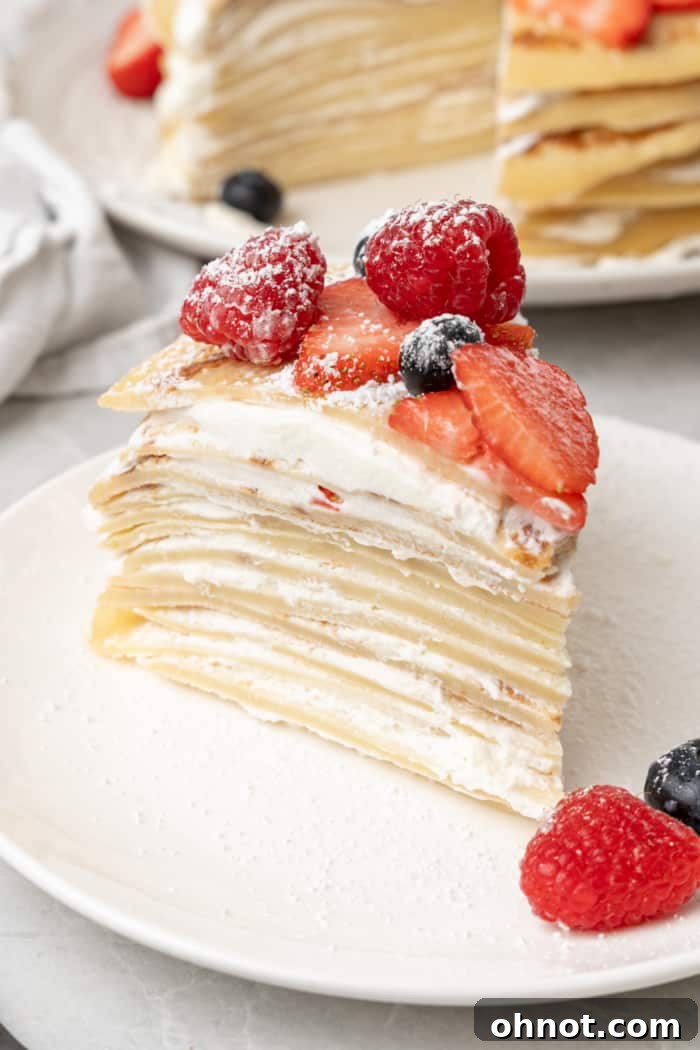 A slice of elegant crepe cake on a plate, revealing its layers, garnished with fresh berries and a mint leaf.