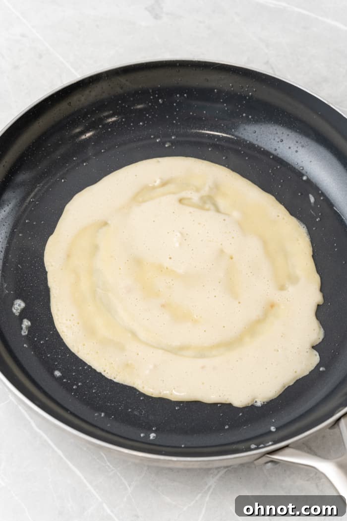 Crepe batter being swirled in a non-stick skillet to create a thin, even layer.