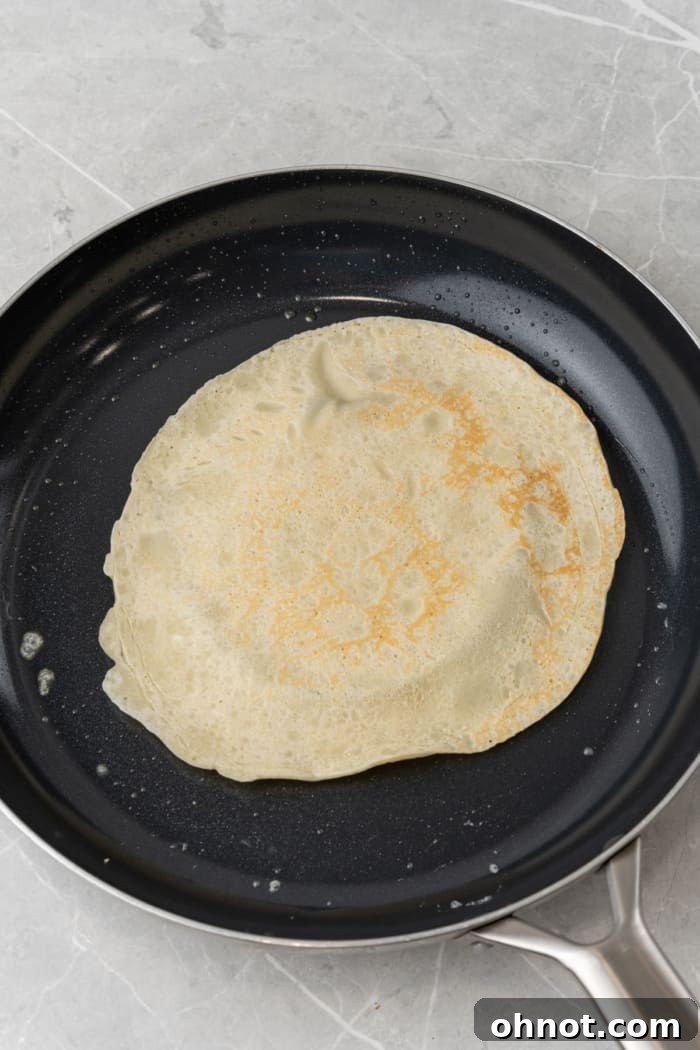 A thin, perfectly cooked pancake (crepe) in a pan, with golden-brown edges.