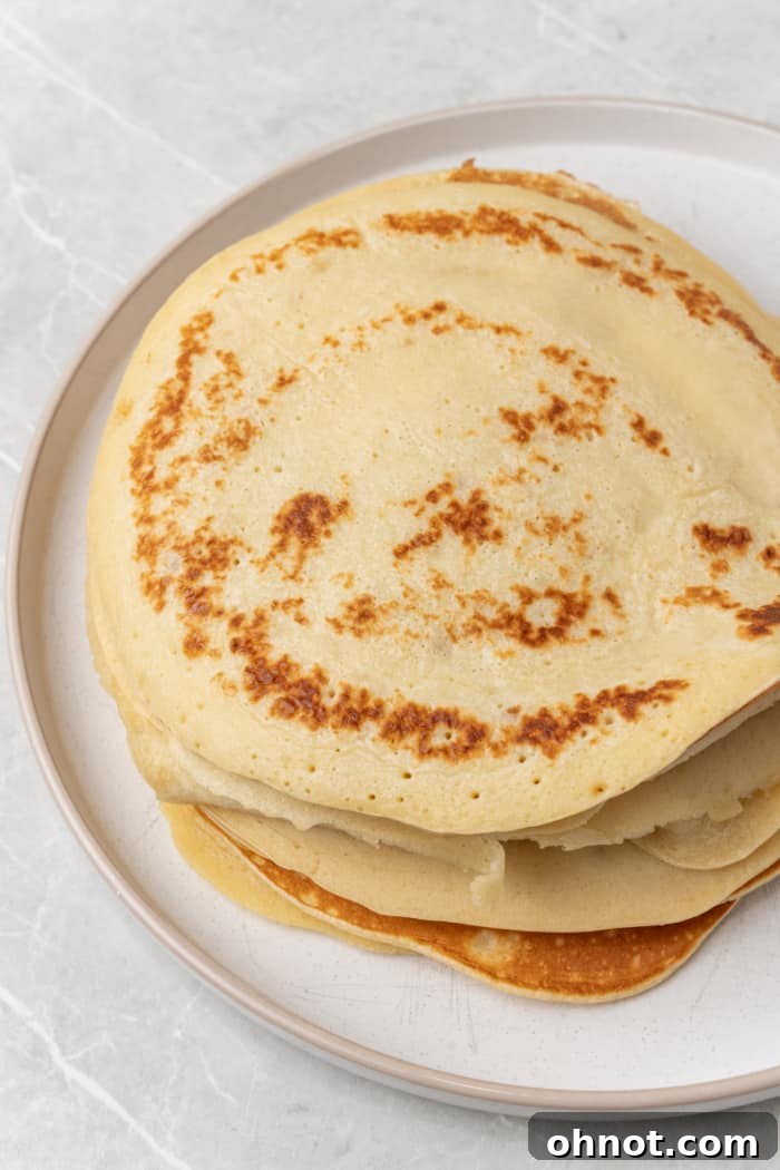 A perfectly stacked pile of thin pancakes (crepes) cooling on a plate.