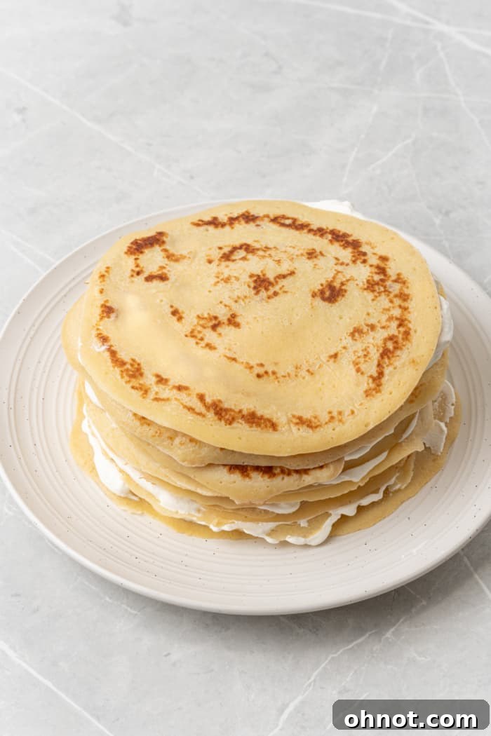 A partially assembled stack of thin pancakes (crepes) layered with whipped cream, showing the progress of the crepe cake.