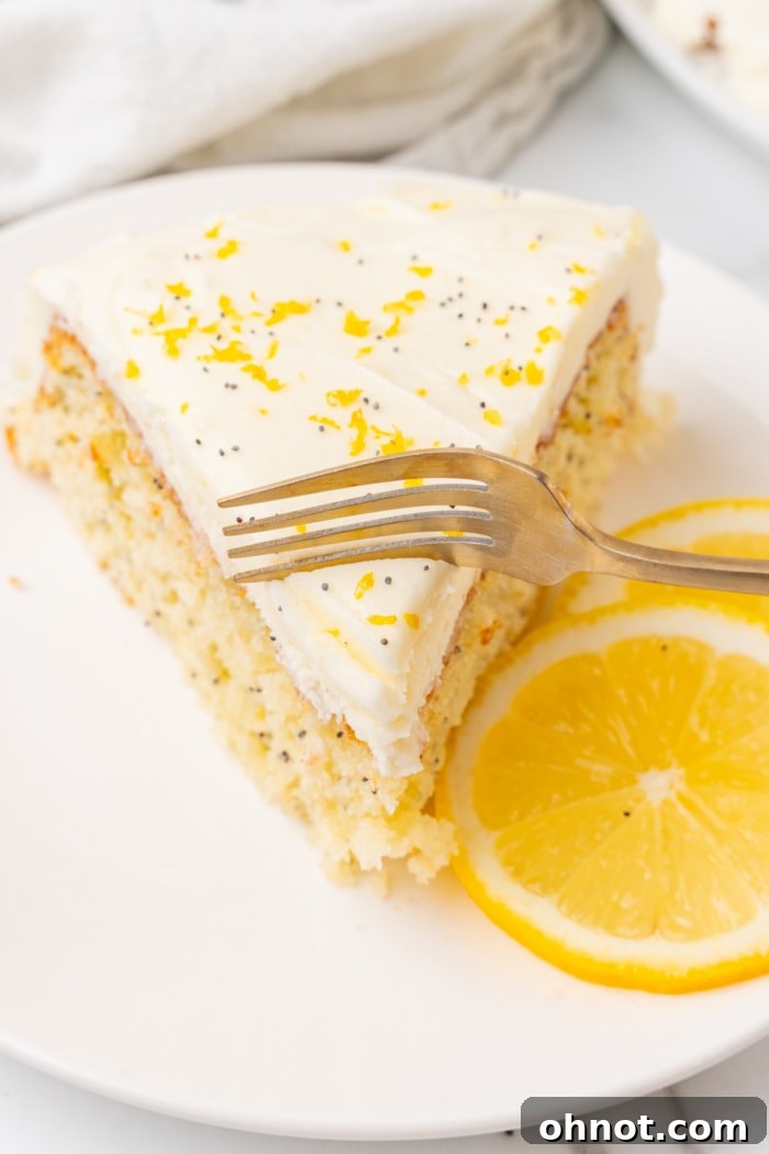 A fork taking a bite from a slice of lemon poppy seed cake.