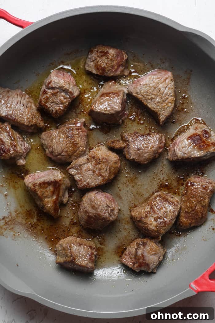 Seared beef in a skillet, developing a rich crust.