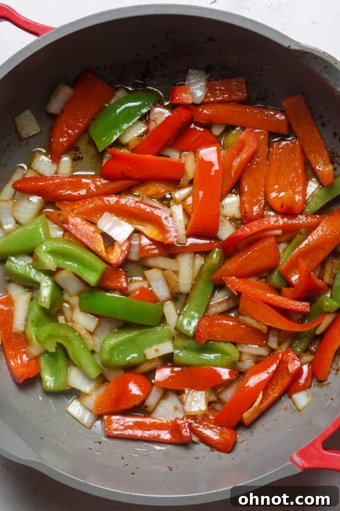Peppers and onions sautéing in a skillet.