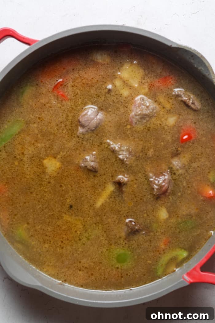 Beef, veggies, and gravy simmering in a pan.