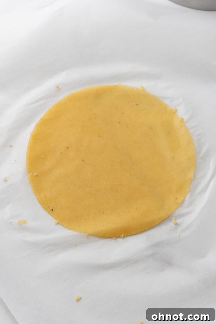A round, thinly rolled almond flour tortilla dough neatly placed between two sheets of parchment paper.