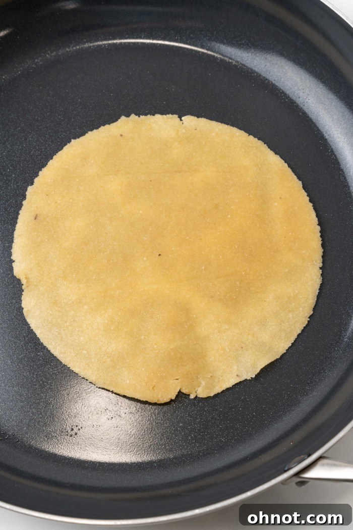 Circular almond flour tortilla dough cooking in a hot non-stick skillet, starting to brown.