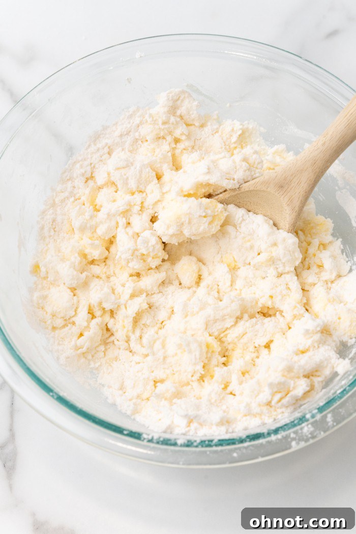Thick, crumbly dough for gluten free biscuits forming in a glass bowl.