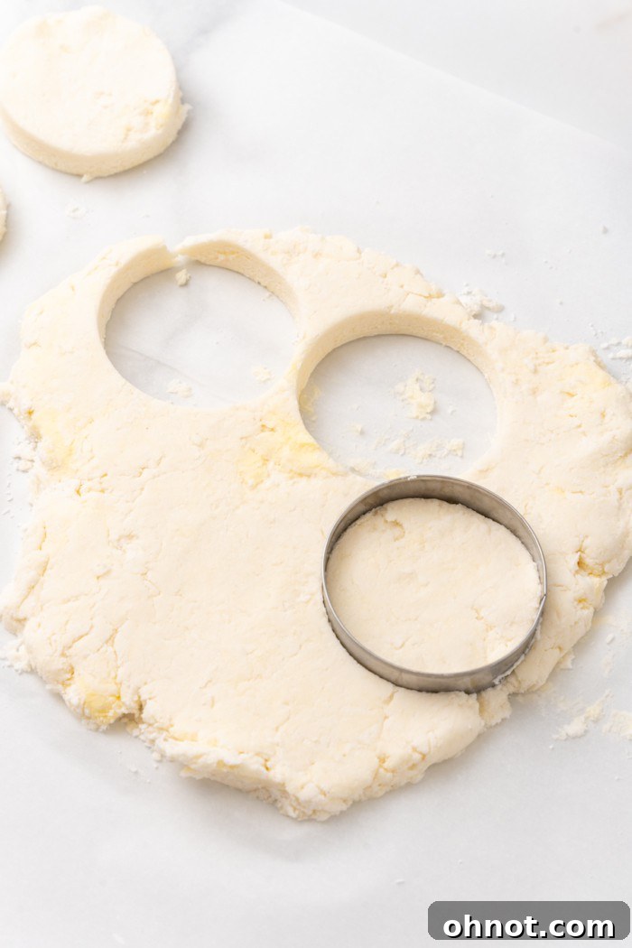 A round biscuit cutter pressing into dough on a floured surface.