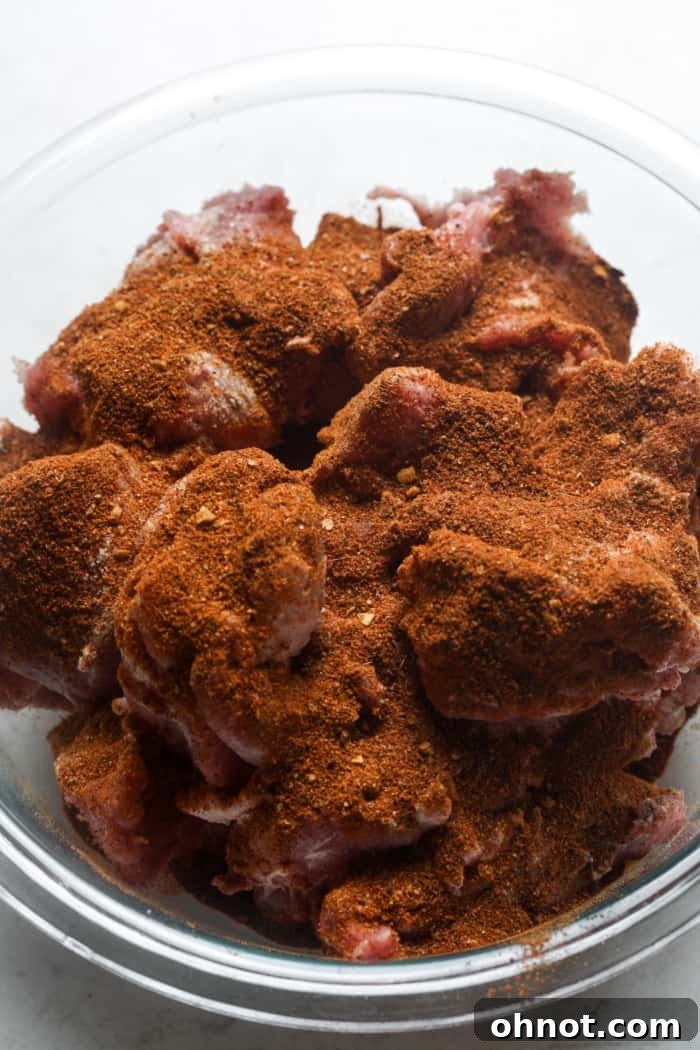 Cubed pork seasoned with spices in a large mixing bowl.