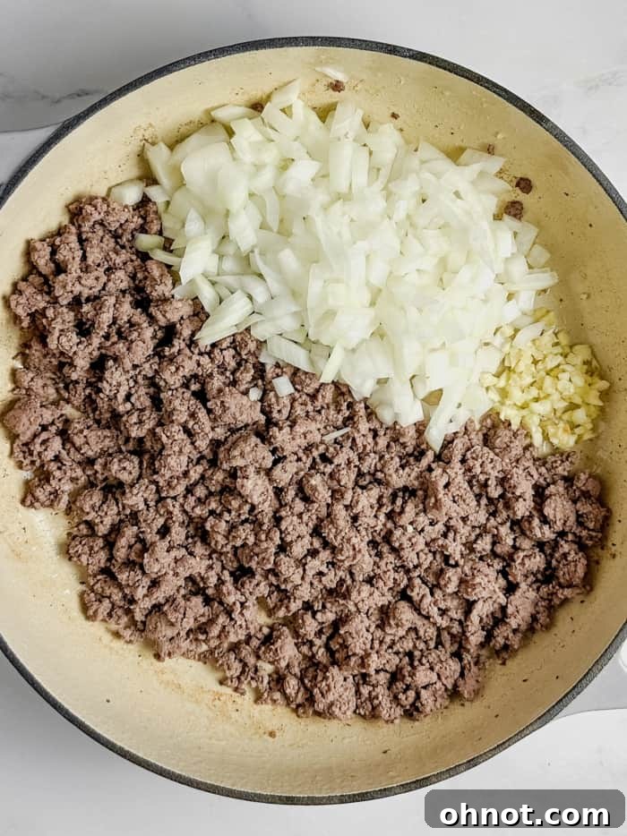 Ground beef mixed with sautéed onions and garlic in a skillet.