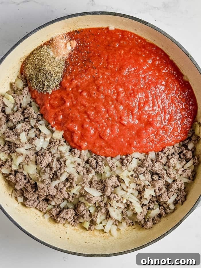 Meat sauce simmering in a skillet with marinara, herbs, and spices.