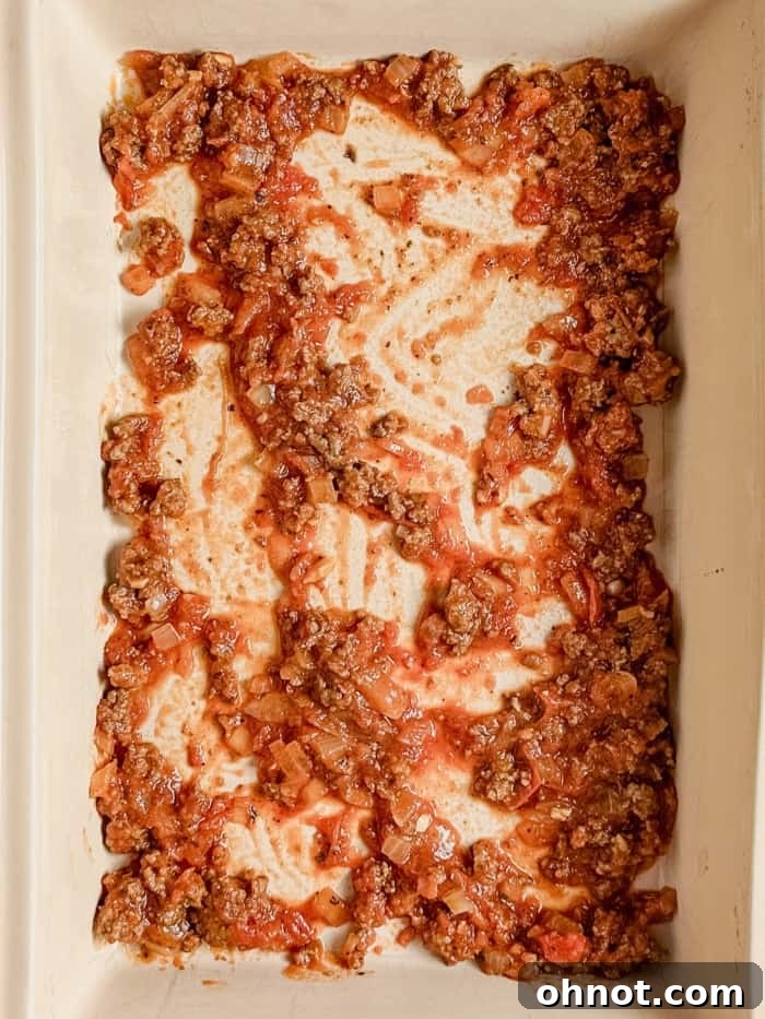 A thin layer of meat sauce spread evenly at the bottom of a baking dish.