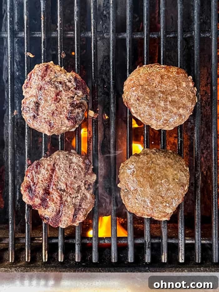 Two hamburger patties sizzling on a hot grill, showing grill marks.