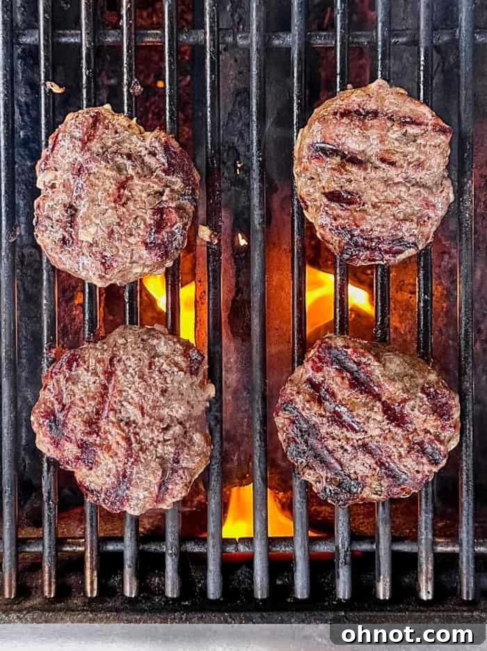 Two perfectly grilled hamburger patties with visible char marks, resting on the grill.