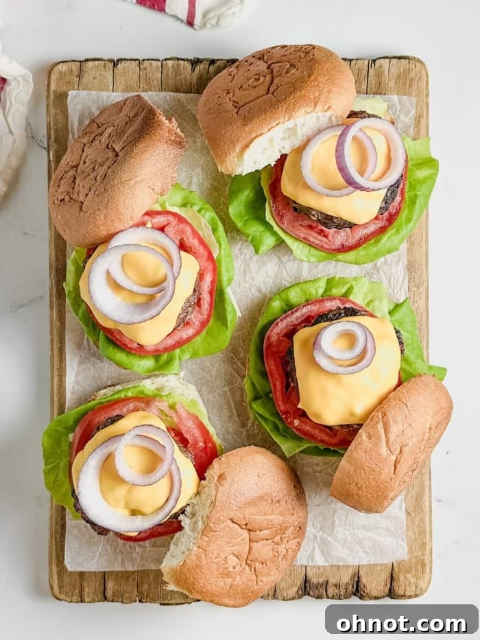 A platter featuring several gluten-free burgers, each topped with melted cheese, lettuce, tomato, and onion, ready to be served.
