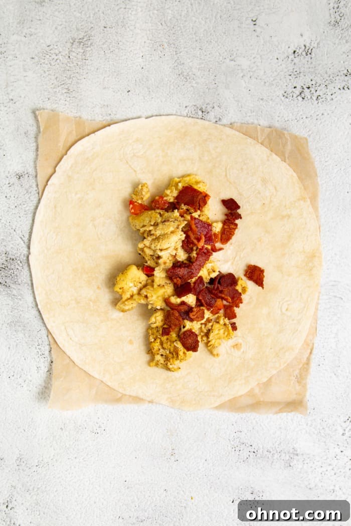 A tortilla being filled with scrambled eggs and cooked bacon pieces.