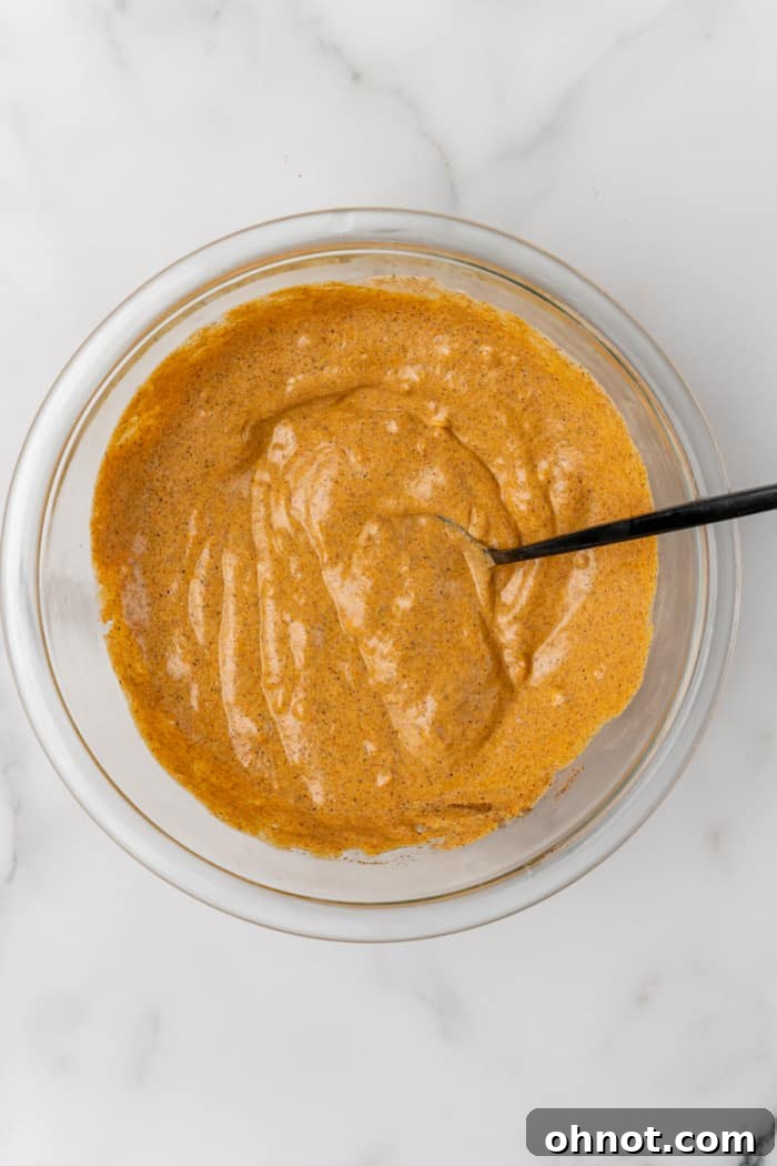 A large bowl filled with an orange-red Indian marinade, rich with spices and yogurt.
