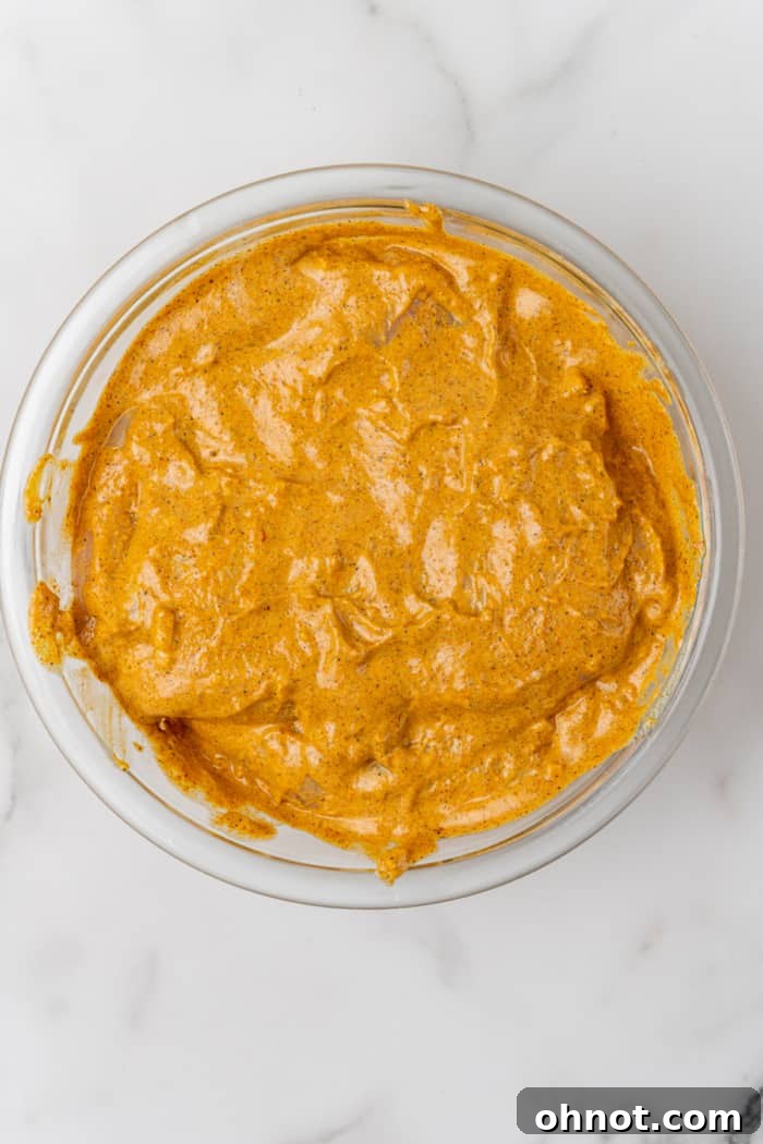 A bowl of chicken pieces coated in a rich orange marinade, ready for refrigeration.