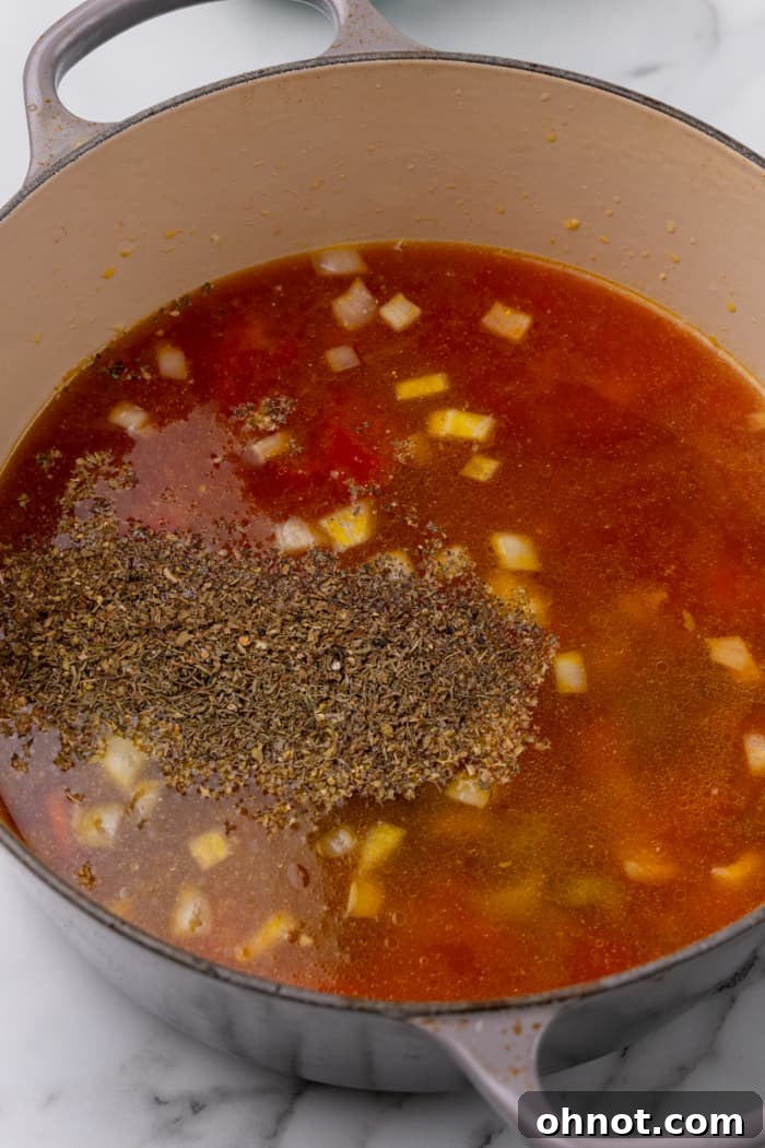 Rich broth, diced tomatoes, and aromatic seasonings added to the sautéed vegetables in a Dutch oven, ready to simmer.