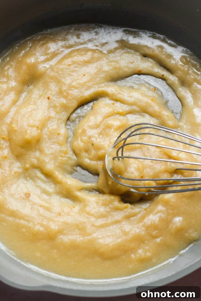 A whisk actively stirring gravy in a pan to prevent lumps.