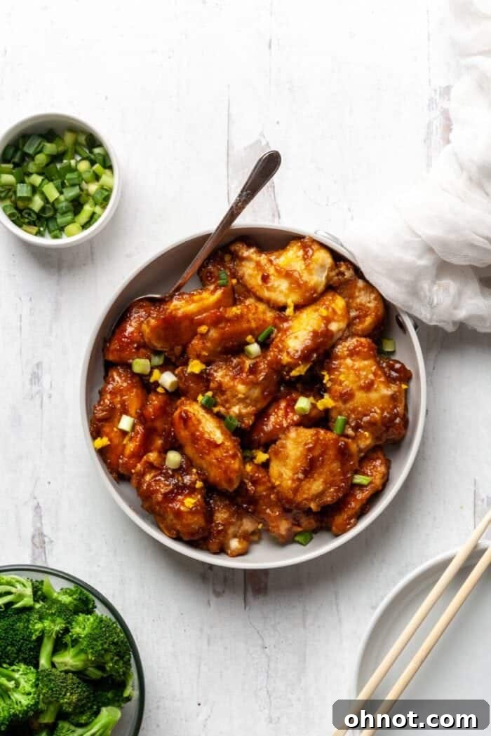 Close-up shot of cooked Whole30 Orange Chicken in a skillet, coated in a thick, glossy orange sauce, ready to be served.