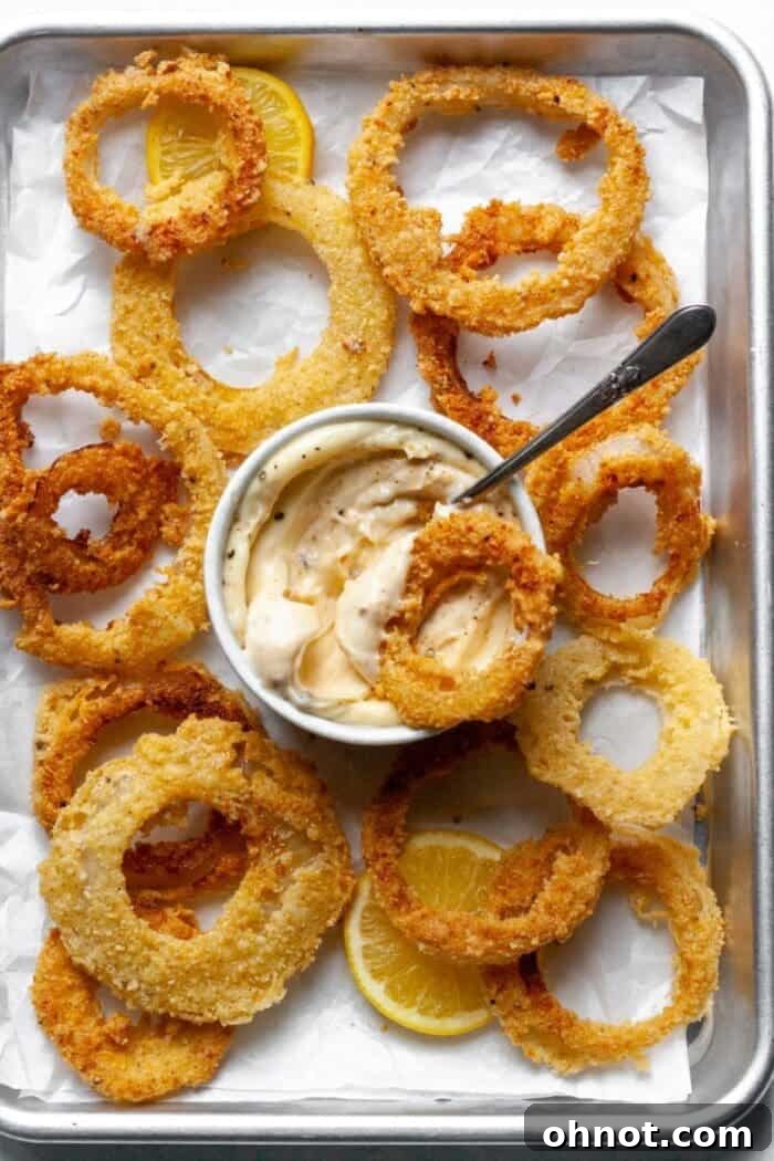 Onion rings on a baking pan with parchment paper and a garlic dip.
