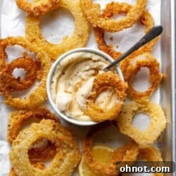 Onion rings on a baking pan with parchment paper and a garlic dip.