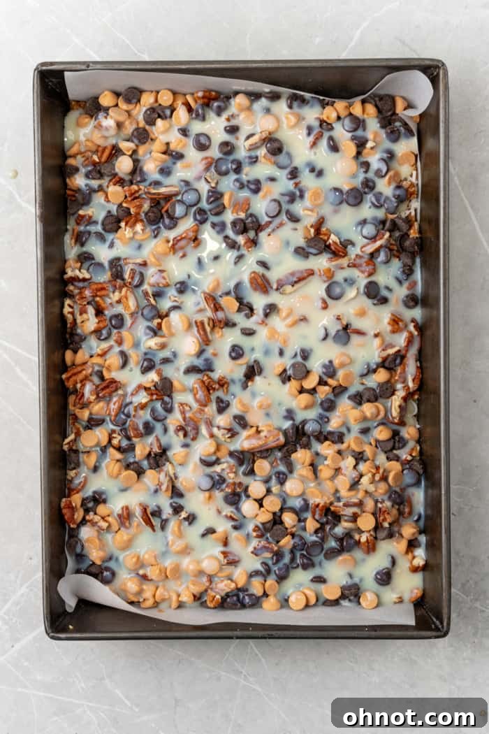 Sweetened condensed milk poured over the layers of chocolate, coconut, and pecans in a pan.