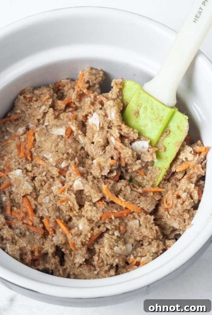 A large mixing bowl filled with thick carrot cake cookie dough, showing shredded carrots and coconut flakes.