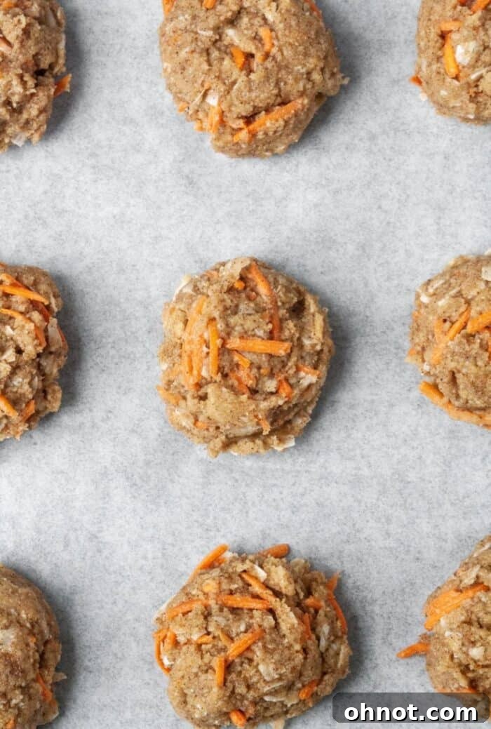 Evenly spaced balls of carrot cake cookie dough on a parchment-lined baking sheet, ready for baking.