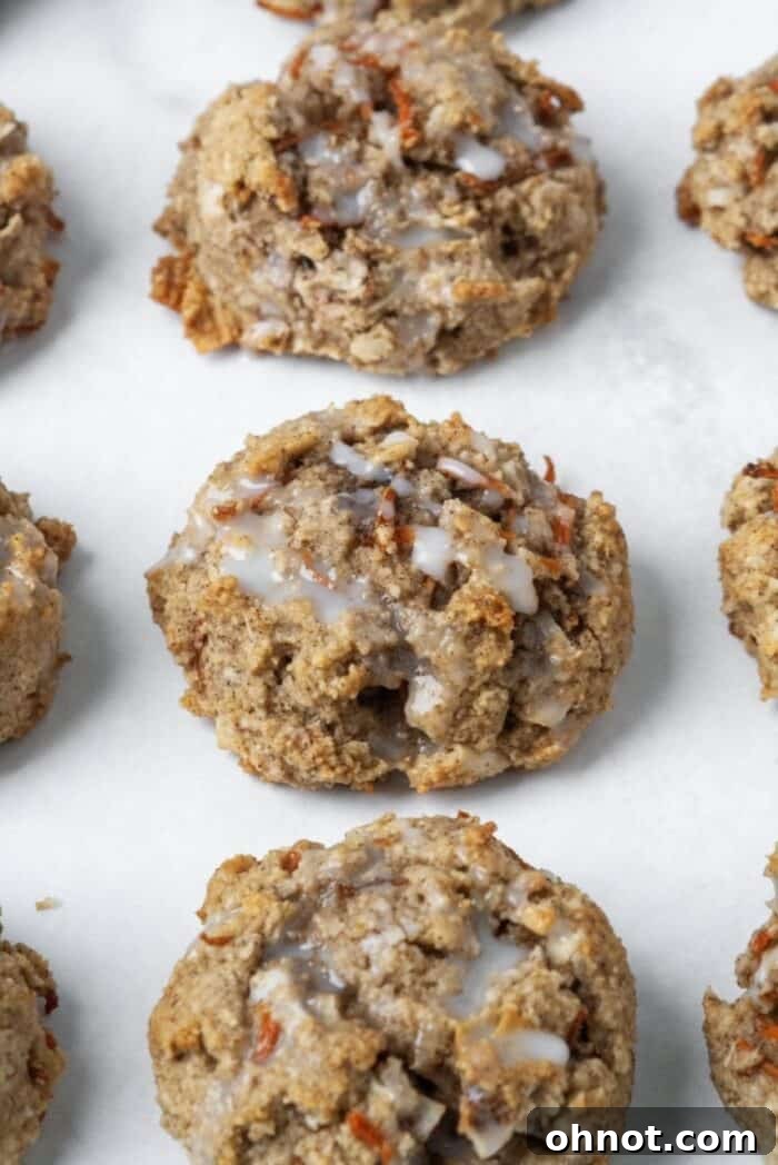 Three glazed carrot cake cookies stacked on a white plate, showcasing the white coconut butter drizzle.