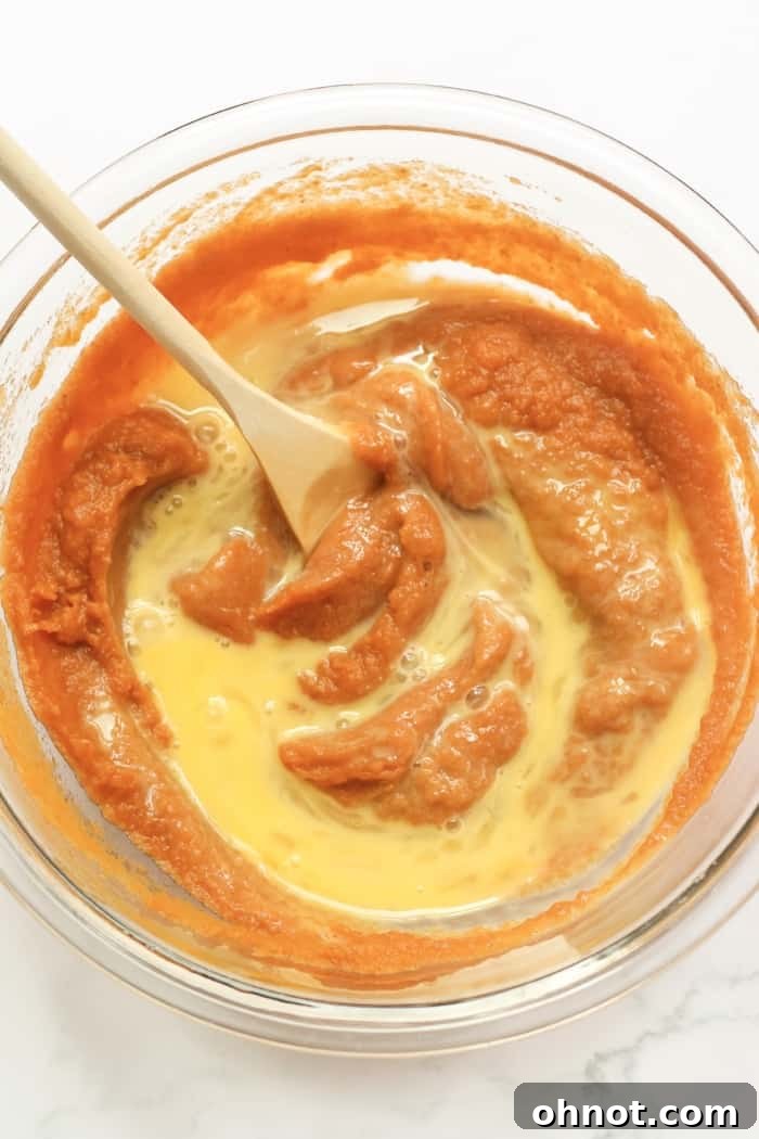 Beaten eggs being added to the pumpkin purée mixture, a key step in creating the creamy healthy pumpkin pie filling.