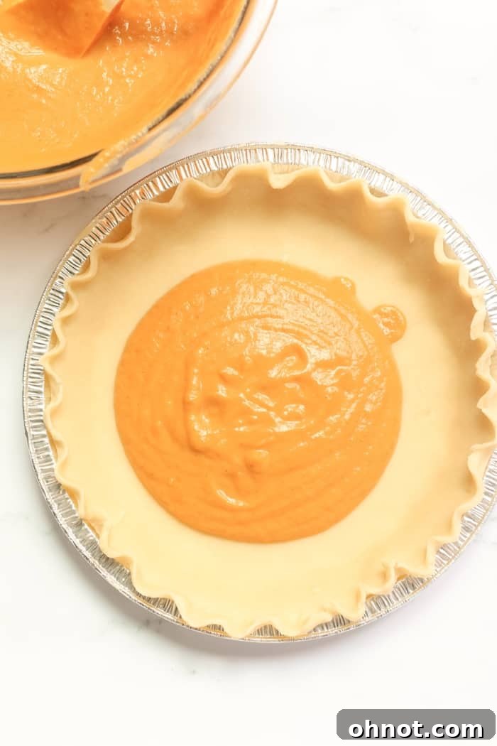 A pie crust being filled with the rich, orange pumpkin mixture for a healthy pumpkin pie.