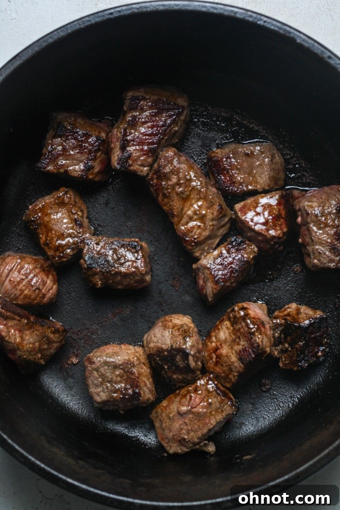 Browned beef sizzling in a skillet, creating a flavorful base.