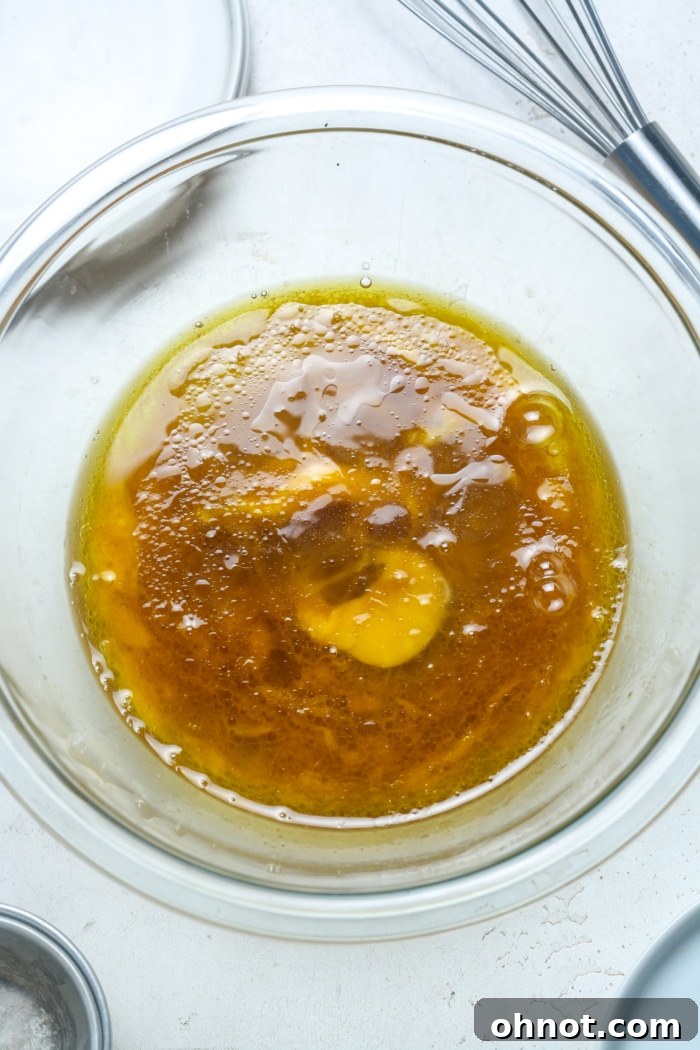 A mixing bowl with golden liquid ingredients: oil, maple syrup, and eggs, ready to be combined with dry ingredients.