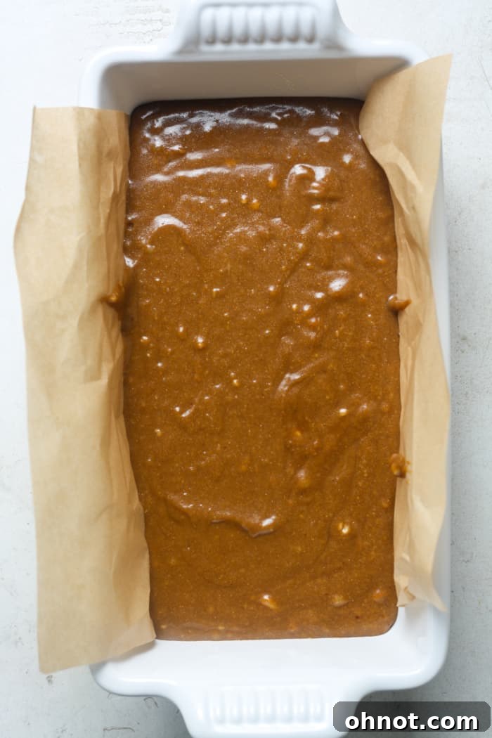 Gingerbread batter perfectly spread in a parchment-lined loaf pan, ready for baking.