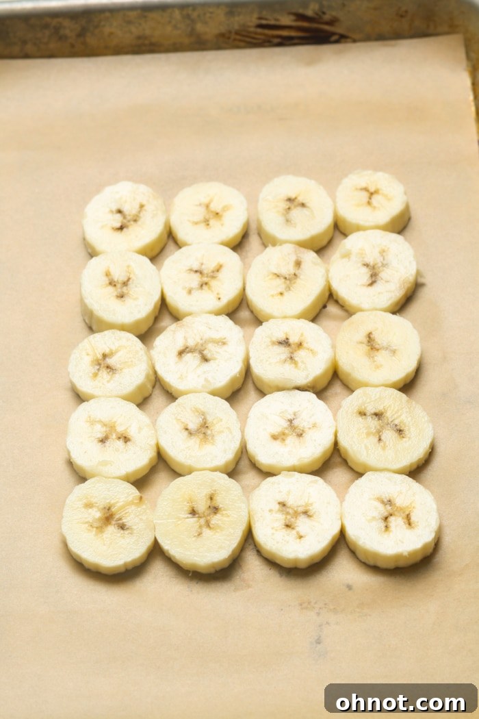 Evenly sliced bananas laid out on a baking sheet with parchment paper.